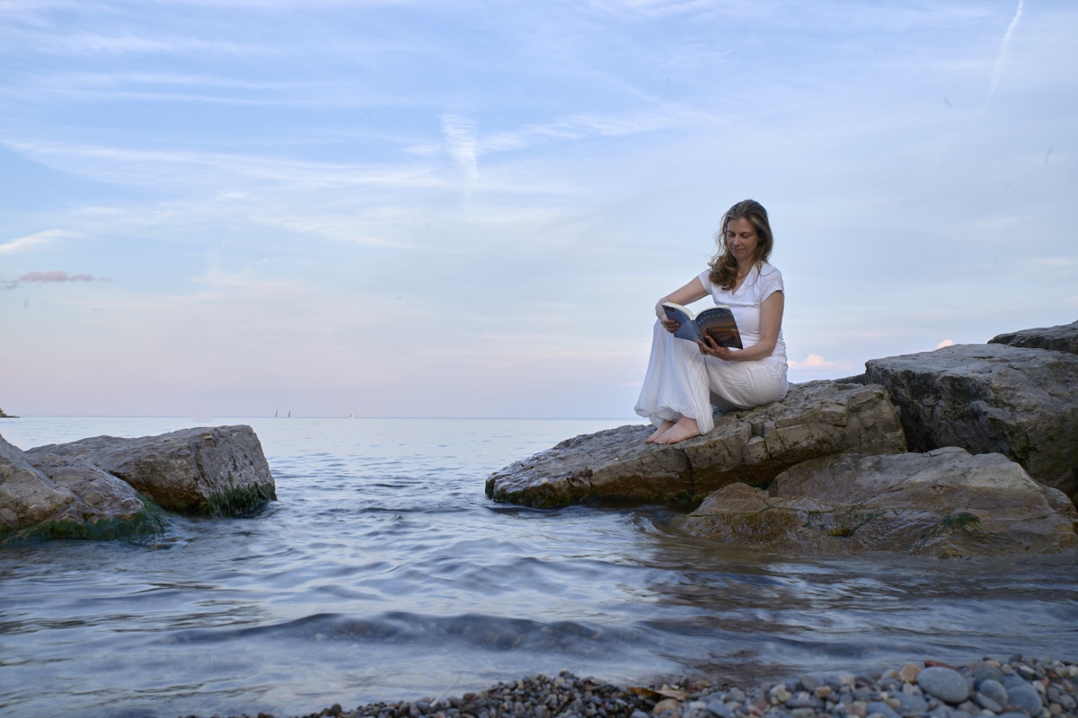 Julia Arbuckle reading on the rocks beside Lake Ontario.